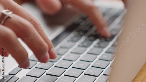Freelancer composing article on wooden desk. Individual typing on keyboard with rings in warm sunlight. Creative writer concentrating on article at hotel workspace with sunlight and rings