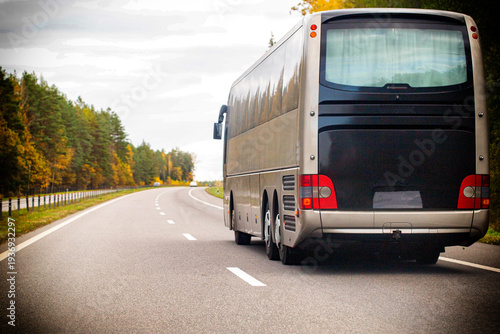 Rear view of touring coach bus driving on winding road through forest during autumn day with overcast sky, journey concept