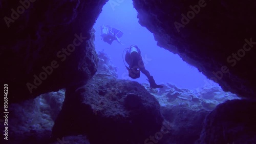 following lookout from a dark triangle cave to two divers in front diving coming out from the cave while scuba diving in the deep ocean sea salt water underwater world during day time in Lanyu Taiwan 