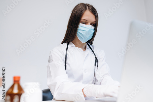 Φωτογραφία Female doctor wearing mask and gloves working on a computer in clinic for teleme