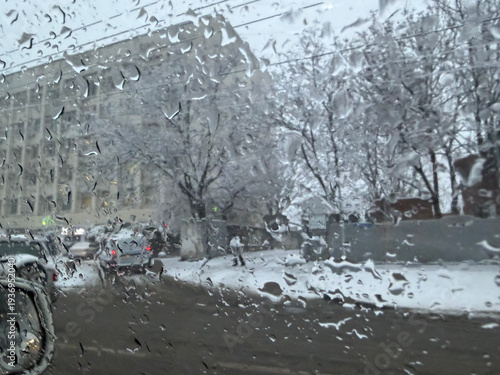 Billede på lærred Raindrops on car window during snowy day in city