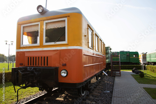 Historic orange and cream railcar displayed at an outdoor museum on a sunny day in a park setting