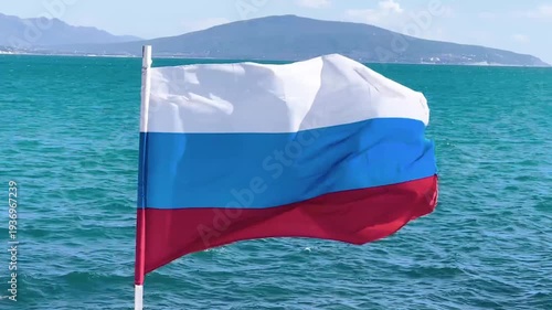 National flag of russia fluttering against a blue sea and mountains on a sunny summer day