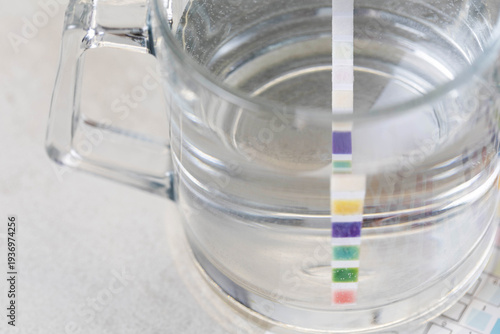 Water quality test strip dipping in glass of water showing chemical reaction for measurement of various parameters of water purity and composition