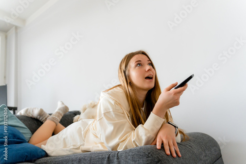 Young Woman Watching TV with Remote Control on Sofa