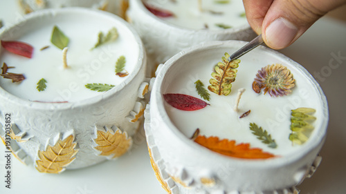 Photos The master's male hand decorates scented candles with colored leaves with tweezers