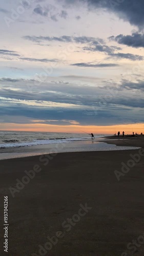 Silhouette of Men Fishing from Sandy Beach at Evening Sunset a Summer Day