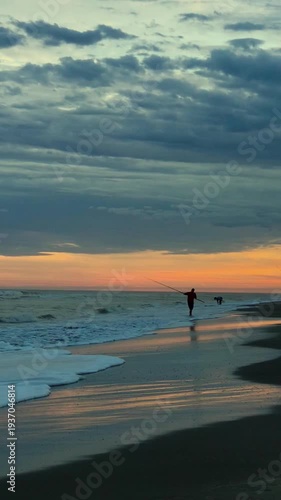 Man Fishing at Shore on Beach at Dramatic Colorful Sunset with Clouds