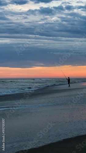 Man Fishing at Shore on Beach at Dramatic Colorful Sunset with Clouds