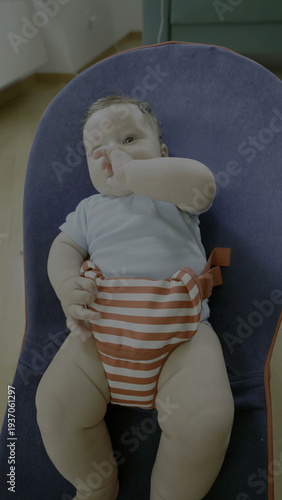 Obraz na plátně Baby sitting on bouncer chair, looking up with wide-eyed expression, lips slight