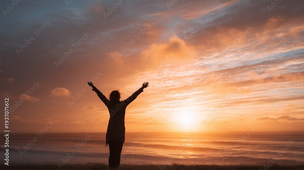 Fototapeta premium Silhouette of person standing with arms outstretched embracing a breathtaking sunset over ocean horizon