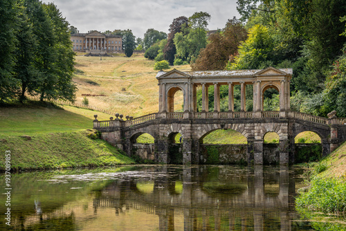 The Palladian Bridge perfectly reflected in the water amidst the lush greenery of Prior Park, Bath, England