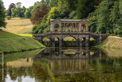 The Palladian Bridge perfectly reflected in the water amidst the lush greenery of Prior Park, Bath, England