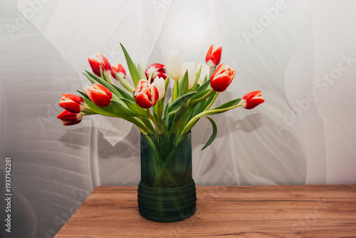Bouquet of beautiful tulips in vase on wooden table against light green background