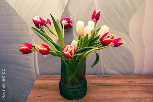 Bouquet of beautiful tulips in vase on wooden table against light green background