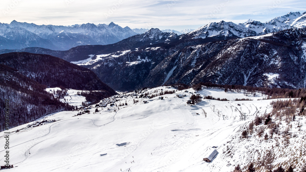 Obraz premium Aerial panorama of a snowy alpine valley with a small mountain village surrounded by dramatic peaks and winter landscapes