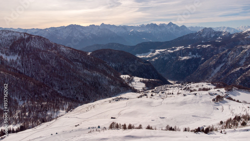 Aerial panorama of a snowy alpine valley with a small mountain village surrounded by dramatic peaks and winter landscapes
