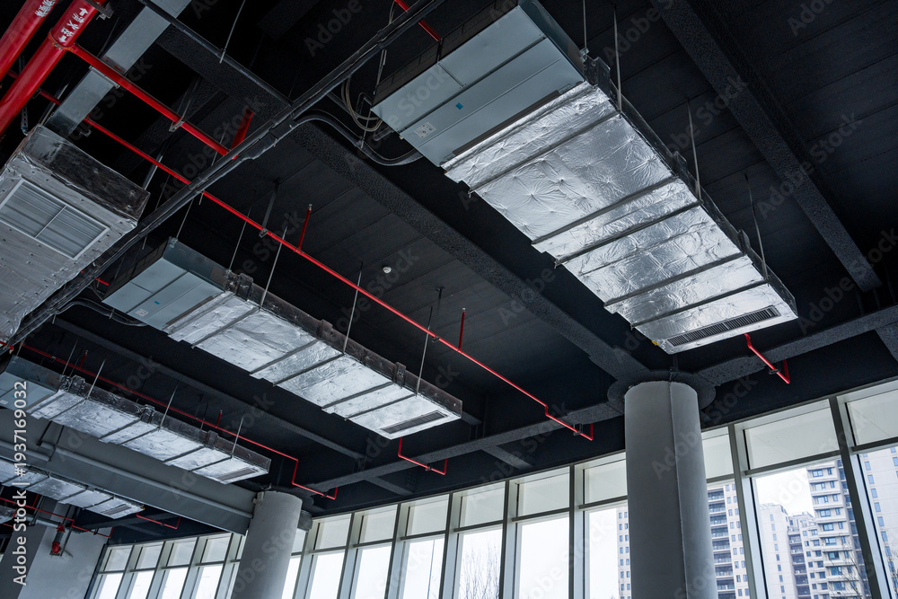 Naklejka premium Industrial-style office interior with exposed ceiling, ventilation ducts, and large windows overlooking the city
