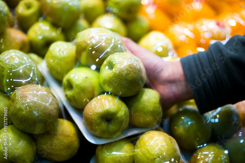 Quadro su tela Green apples wrapped in plastic film displayed on supermarket shelf with hand se