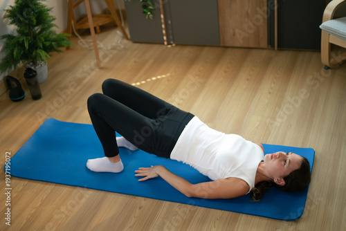 Female practicing glute bridge exercise on yoga mat indoors
