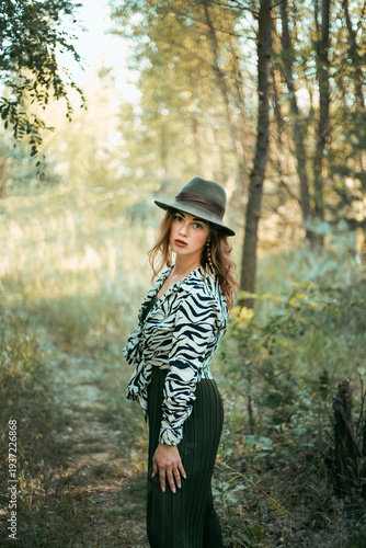 Model poses in nature wearing a zebra print top and hat while surrounded by trees on a sunny day