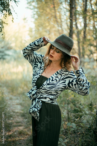 Model poses in nature wearing a zebra print top and hat while surrounded by trees on a sunny day