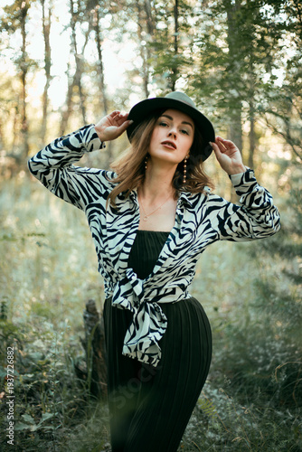 Model poses in nature wearing a zebra print top and hat while surrounded by trees on a sunny day