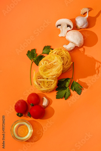 Food ingredients for cooking Italian pasta. Fresh cherry tomatoes, mushrooms, garlic, parsley, olives, spaghetti, olive oil on orange background top view