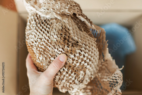 Close-up of a hand holding honeycomb kraft paper protective packaging. The expandable paper wrap with a textured honeycomb structure is used as an eco-friendly alternative to plastic bubble