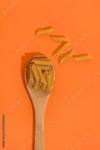 Raw pasta in spoon isolated on orange background, top view