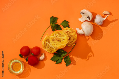 Food ingredients for cooking Italian pasta. Fresh cherry tomatoes, mushrooms, garlic, parsley, olives, spaghetti, olive oil on orange background top view