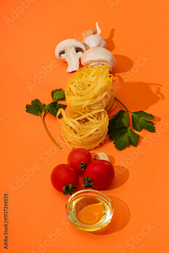 Food ingredients for cooking Italian pasta. Fresh cherry tomatoes, mushrooms, garlic, parsley, olives, spaghetti, olive oil on orange background top view