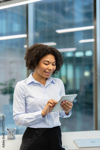 Vertical photo of a smiling young African American businesswoman in the office using a tablet