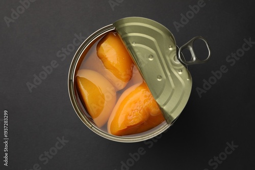 Pickled peaches in tin can on black background, top view