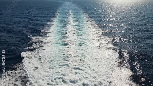 View from the stern of a ship showing the foamy wake trailing behind on the deep blue ocean.