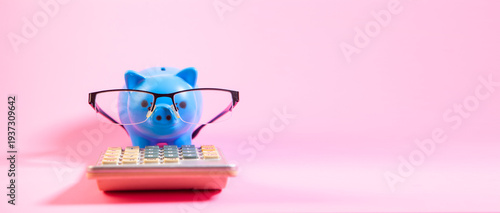 Piggy bank with eyeglasses and calculator on pink background