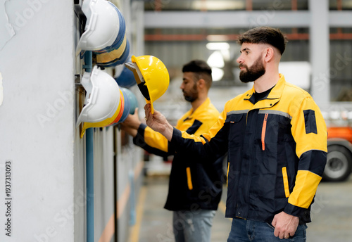 Tablou pe pânză Industrial worker selecting safety helmet from PPE rack in factory warehouse