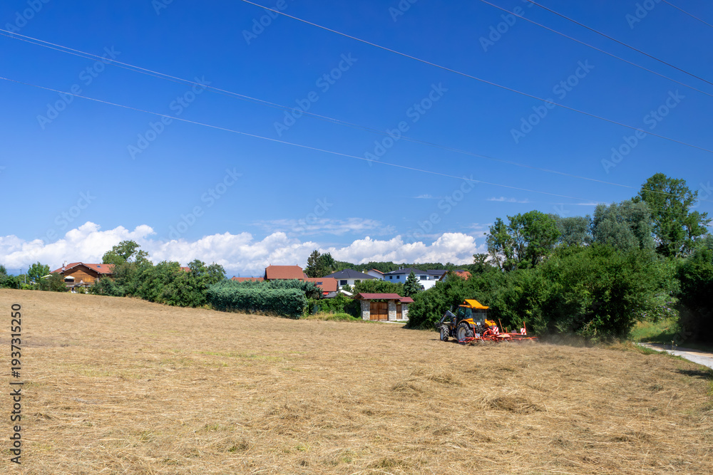 Fototapeta premium Tractor working in harvested field near rural village