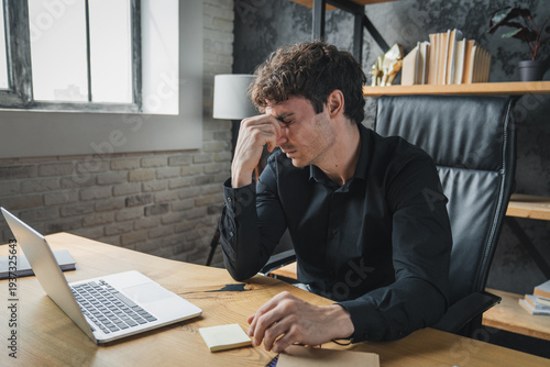 Tired businessman taking off glasses, massaging nose bridge leaning back in chair at workplace, overworked man suffering from computer vision syndrome after long laptop use, eye strain problem