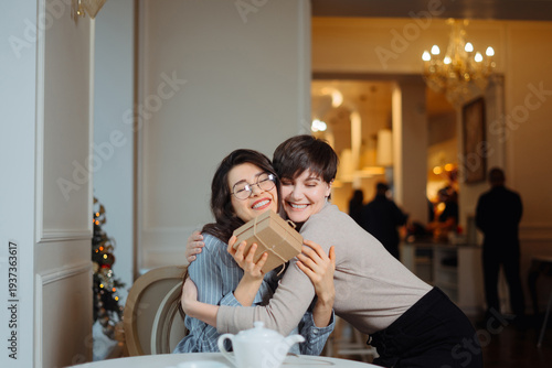 Foto Young beautiful girl sitting in cafe with her friend and receiving a gift