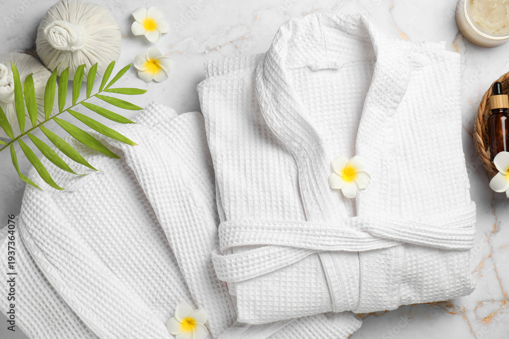 Fototapeta premium Flat lay composition with bathrobes and spa products on white marble table