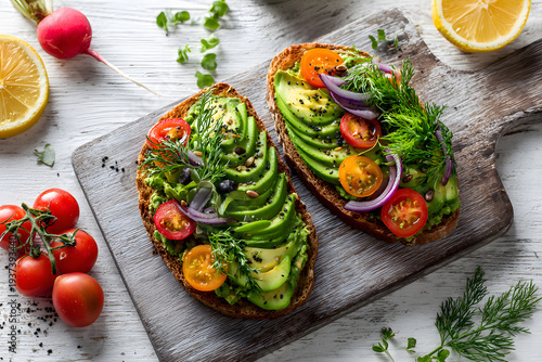 Healthy toast with avocado, tomatoes, and herbs on a wooden board in a bright kitchen setting