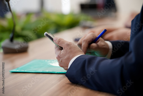 Bild auf Leinwand Side view of a manager in a blue suit using a mobile phone and holding a pen