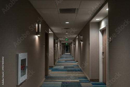 Long hotel hallway with room doors, lighting, and exit signs.