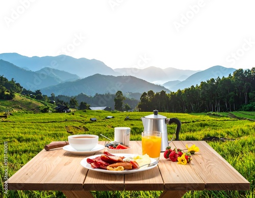 Outdoor breakfast with mountains. A wooden table displays food amidst a grassy field and layered mountains beyond