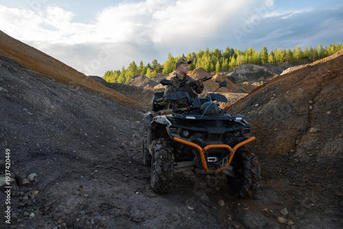 Armed Soldier Standing Near ATV in Rugged Quarry Landscape