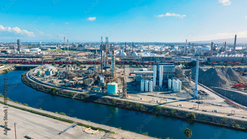 Fototapeta premium Aerial view of oil refinery featuring distillation towers and storage tanks along the riverbank in a bustling industrial area