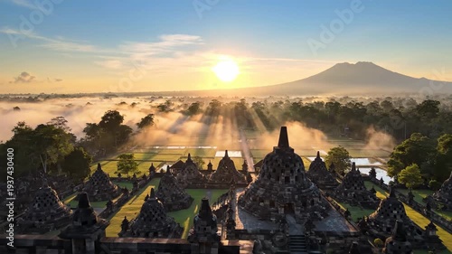 A temple complex at sunrise, enveloped in mist, with a mountain backdrop and radiant light rays breaking through