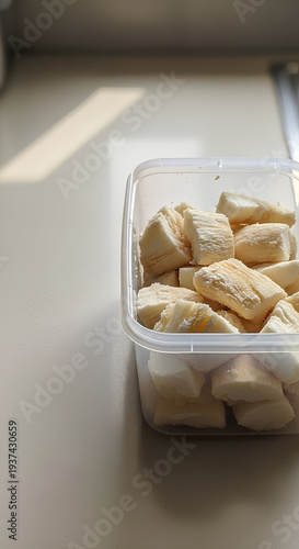 Plain plastic tub with fermented cassava pieces placed in the right third of a light beige countertop, large empty left side acting as negative space for cultural or fermentation copy.