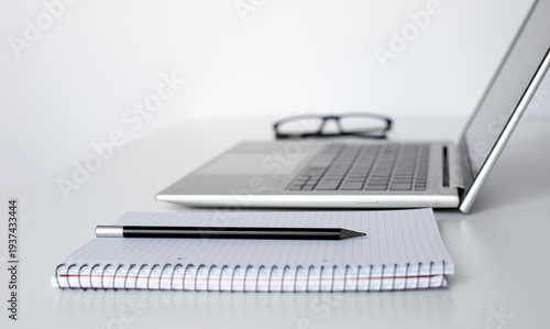 Stylish office space with a laptop placed next to  a spiral notebook, glasses, and a pen. A clean and elegant business composition.